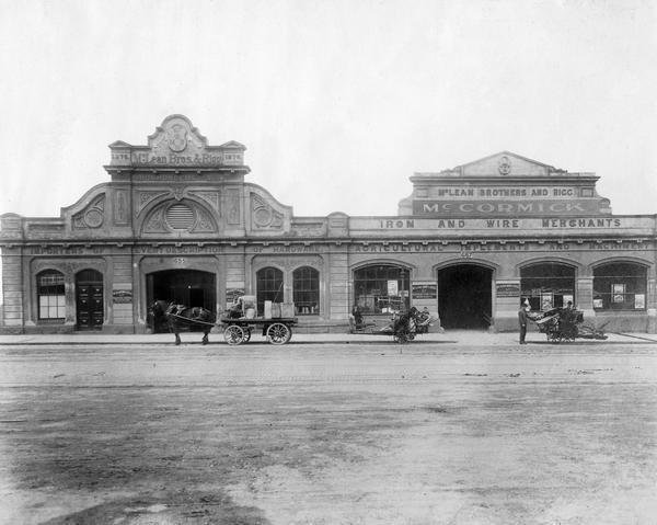 McCormick Harvesting Machine Company dealership building owned by McLean Brothers and Rigg, Ltd. of Melbourne, Australia. Men are standing in the street in front of the dealership with a horse-drawn wagon loaded with goods and two McCormick binders.