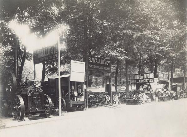 Agricultural machinery on display in an exhibition by R. Wallut & Co. of Paris, France. Signs advertise Hornsby oil engines, cream separators and "mills of the future for agriculture."