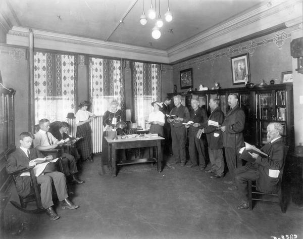Factory workers reading in the Deering Works Club library. A librarian appears to be checking books in and out to a line of employees.
