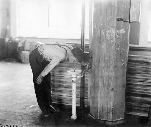 Factory worker drinking from a water fountain inside International Harvester's Deering Works.