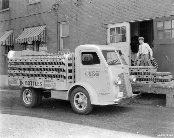 Delivery man loading bottle cases of Coca-Cola soda onto the open bed of an International C-300 delivery truck.