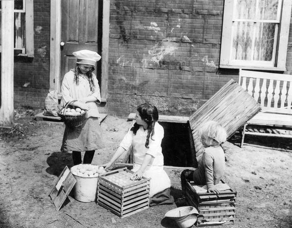 Young children crating fresh eggs in front of a farmhouse.
