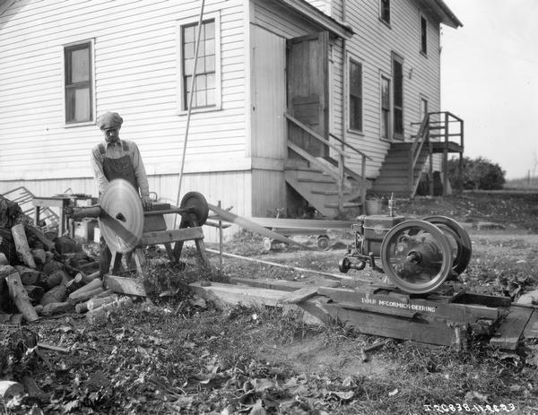 Farmer, possibly Walter Stange, cutting wood with a circular saw run by a 1 1/2 H.P. Type M McCormick-Deering gas engine.