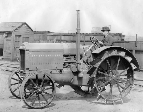 Engineering photograph of an experimental McCormick-Deering 15-30 tractor taken in a factory rail yard. A man in a suit and hat is sitting at the wheel of the tractor.