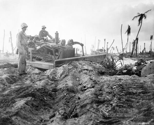 Two U.S. Marines using an International TD-9 diesel TracTracTor (crawler tractor) and bulldozer to search for Japanese soldiers on Namur, Kwajalein Atoll, Marshall Islands. Original caption reads: "The Jap pill boxes were buried so well only a bulldozer could rout them out."