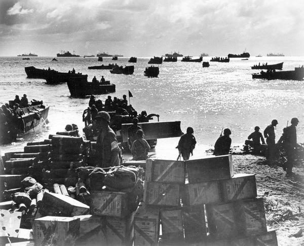 Original caption reads: "Coast guardsmen shuttle landing craft back and forth from the anchorage to the beach of Eniwetok Atoll, bringing in fighters and supplies, carrying back the wounded. On the beach supply dumps swiftly pile up. An International TD-9 diesel TracTracTor [crawler tractor] is coming ashore." Official Coast Guard Photo.