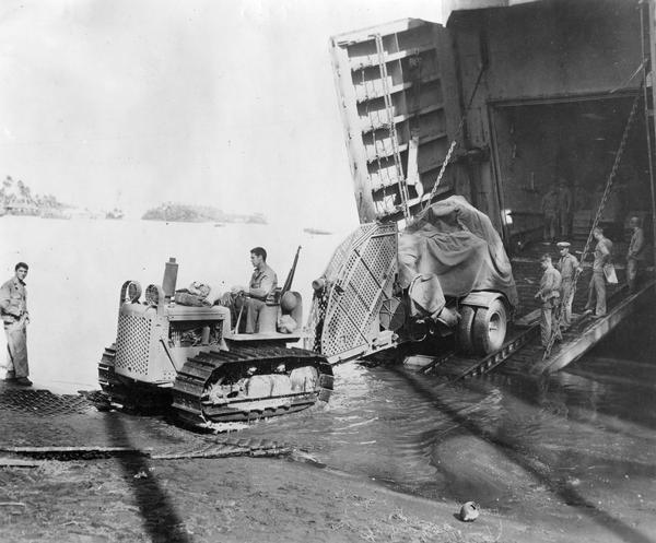 U.S. Marines using an International Harvester TD-9 diesel TracTracTor to unload a field gun from an LST boat on the beach at Rendova. Original caption reads: "This gun and others like it pounded away at Munda across the channel on New Georgia Island until the Japs fled. The LST's, because of their size and color, are known to the Marines as Green Dragons."