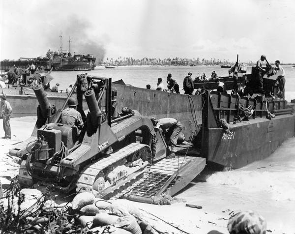 U.S. Marines using an International TD-9 diesel TracTracTor (crawler tractor) with a Bucyrus Erie shovel on an LCM (Landing Craft, Materiel) at Roi during the Marshall Island invasion. Original caption reads: "It carries no guns, but the crawler tractor is a highly important 'weapon of war'." Official U.S. Navy photograph.