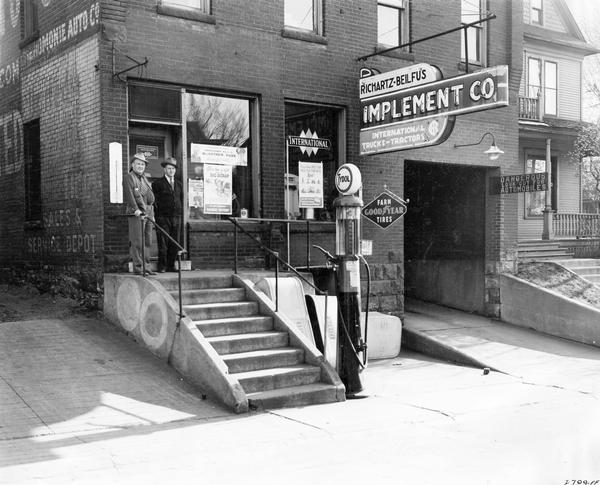 Storefront of the Richartz-Beilfus Implement Co., an International Harvester truck and tractor dealership. At left is W.P. Beilfus, at right is T.C. Richartz. The original caption reads: "These photographs illustrate effective use of posters in windows." The posters feature ads for local and state-wide scrap drives.