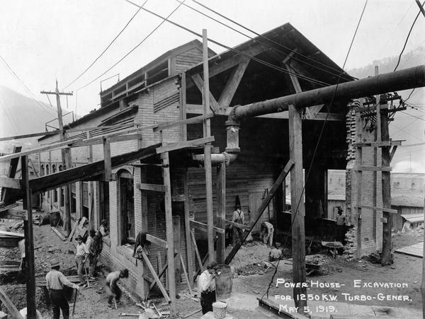 Workers preparing the power house for the addition of a 1250 k.w. turbo generator. A man in the foreground is taking a drink of water from a pail. Benham was a "company town" created by International Harvester for the workers of the Wisconsin Steel Company. Wisconsin Steel was a subsidiary of International Harvester and operated coal mines at Benham.