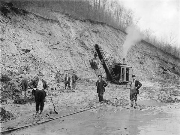 Workers standing outdoors in the mud with a steam shovel. Benham was a "company town" created by International Harvester for the workers of the Wisconsin Steel Company. Wisconsin Steel was a subsidiary of International Harvester and operated coal mines at Benham.