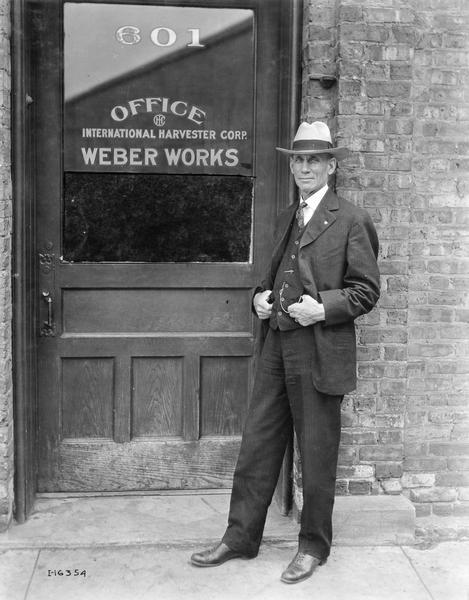 Male office worker, possibly the factory superintendent, posing in front of the office door of International Harvester's Weber Works.