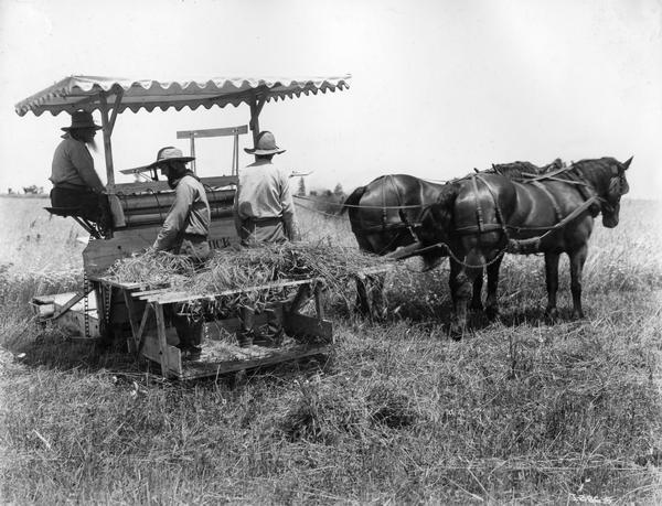 Men demonstrating the horse-drawn McCormick "Marsh type" harvester built ca. 1878. The men are wearing period dress and the photograph was most likely staged as a historical re-enactment - possibly in conjunction with  International Harvester's "reaper centennial" celebration. Original caption reads: "This type of machine was built in McCormick's Reaper Works in Chicago from 1875-1883. An elevator delivered the cut grain to a platform on the side of the machine where it was bound into bundles by hand. Two men could bind the grain as fast as it was cut. With the reapers for earlier years, a crew of 4 or 5 men was required to do the binding."