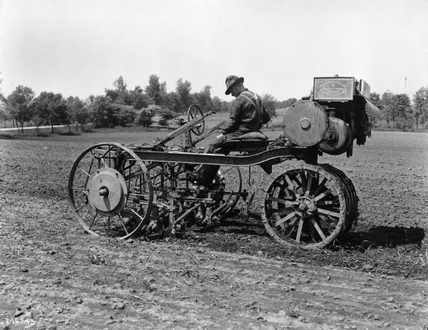 Engineering photograph of a man field testing a limited production motor cultivator. Original caption reads: "... the 1916 motor cultivator with the addition of heavy center weights in the cultivator wheels. These center weights may have been added to strengthen the wheels but there is also evidence that they were an effort to overcome the tendency of the motor cultivator to tip sidewise on hillsides."