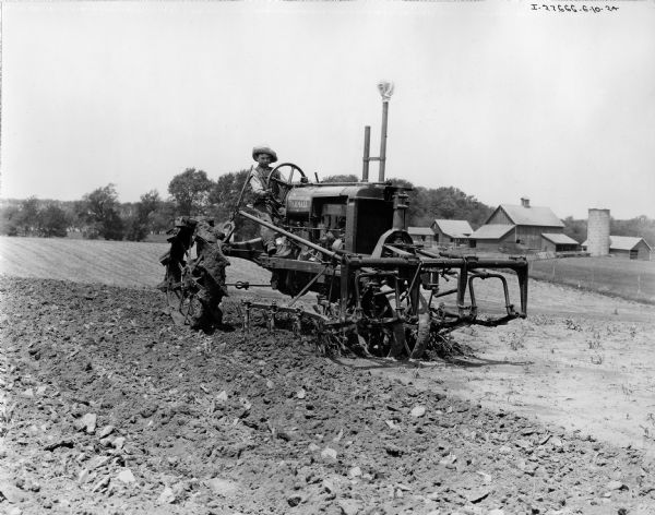 Engineering photograph of young boy cultivating a field with an experimental or early production Farmall tractor with attached cultivator.
