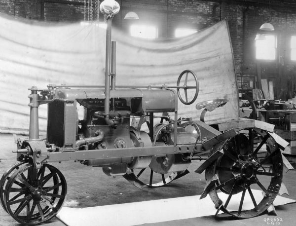 Engineering photograph of an experimental Farmall tractor. A white backdrop is set up along the brick wall in the background.