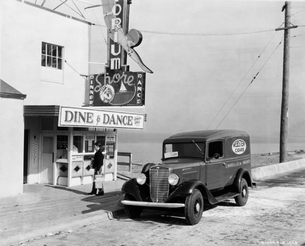 Salesman delivering boxes of cigars to a Seattle diner and dance club. Parked along curb is International C-series delivery truck owned by L. Marks and Co., Inc.