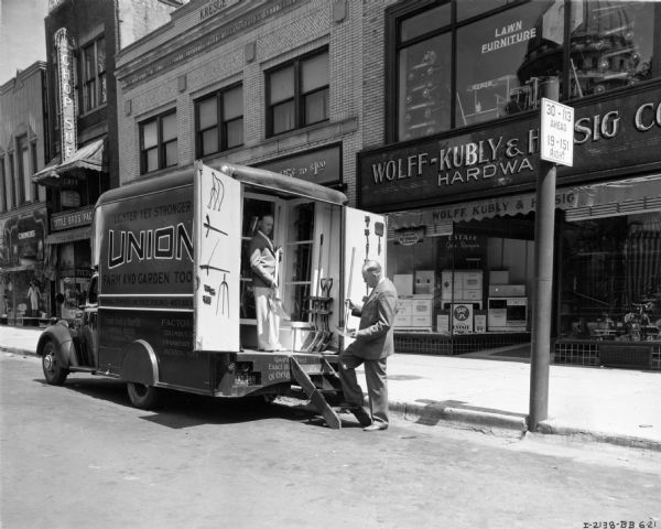 Salesman delivering farm and garden goods to the Wolff-Kubly & Hirsig Hardware store, 21 South Pinckney Street on the Madison Capitol Square, with an International D-15 truck. The truck was owned by Union Fork and Hoe Company, and was equipped with a special body built by Bowne & Bowne of Utica, New York. The Wisconsin State Capitol building is reflected in the glass above the storefront.