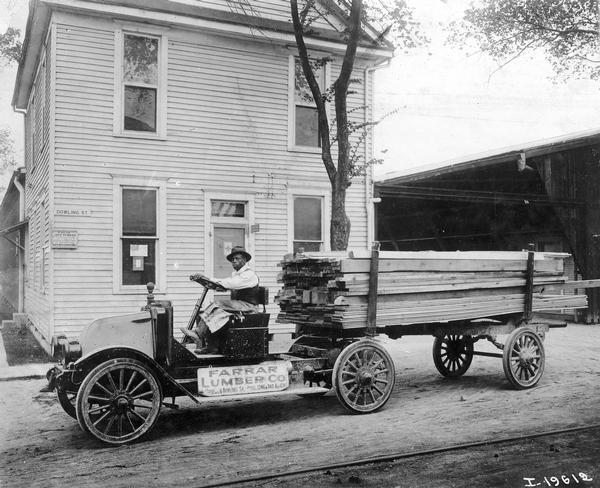 African American driver delivering a load of lumber with an International Model H semi-truck. The truck was owned by Farrar Lumber Company. The company was established by Roy Montgomery Farrar (1870-1943).