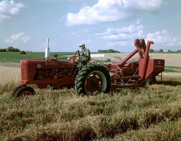 Farmer harvesting grain with a stage I Farmall Super M tractor and McCormick combine (harvester-thresher).