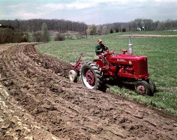 Slightly elevated view of a farmer plowing with a Farmall Super M tractor.
