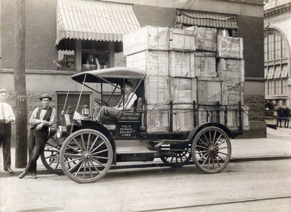 Delivery driver and two other men with an International Auto Wagon Model M loaded with crates. The truck carries the names "Philadelphia and Reading Railway Lines" and "Peipher Line Fast Freight."