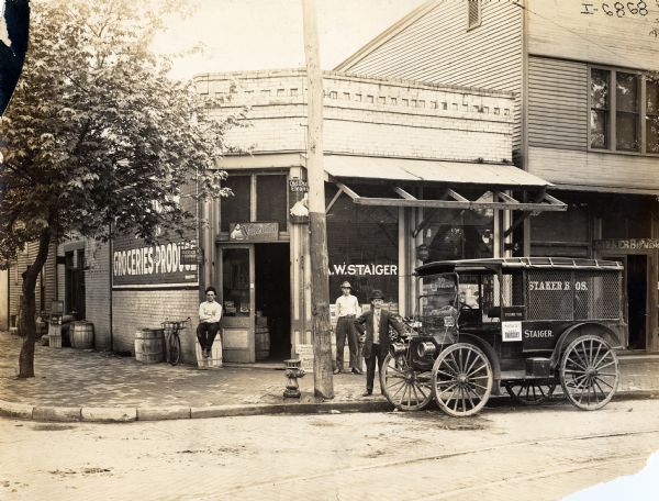Three men and a 1911 International Auto Wagon in front of the grocery store of A.W. Staiger. The store next door is Staker Brothers' meat market.