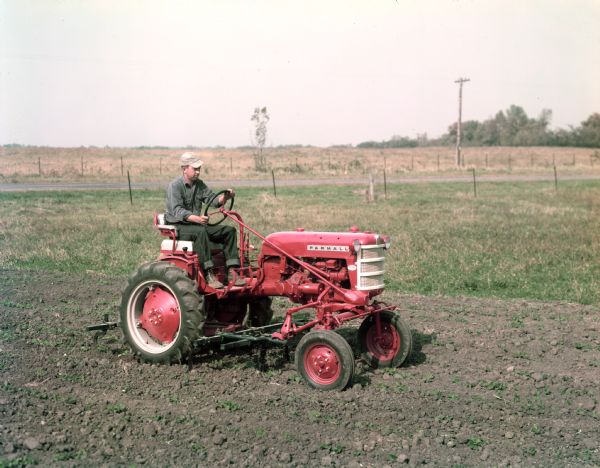 View towards a farmer on a Farmall Cub tractor with attached cultivator.