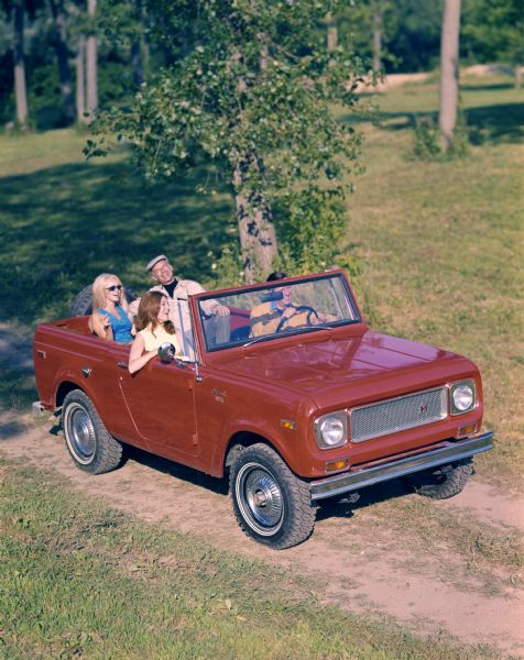 Color advertising photograph of two men and two younger women riding along a rural road in an International Scout convertible pickup.