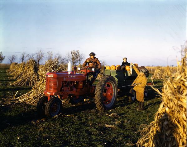 McCormick-Deering Farmall H tractor in a fall setting. A hunter, Mr. Vinson E. Gritten, is holding up a dead rabbit for William Foreman and Junior Scott (boy in wagon). Mr. Foreman is hauling a wagon full of pumpkins.