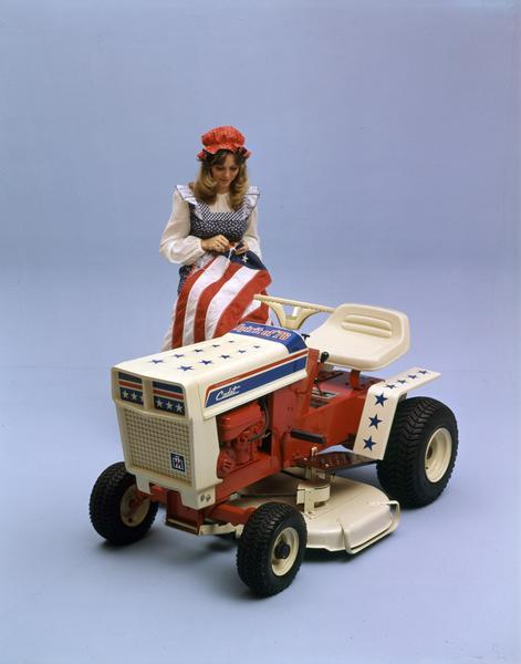 Color advertising photograph for International Spirit of '76 Cadet lawn tractor featuring a model dressed as Betsy Ross sewing stars onto a U.S. flag. The tractor was meant to commemorate the bicentennial of the United States.