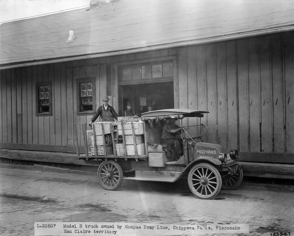Two workers are unloading crates of produce from the back of an International Model H truck. Caption reads: "Model H truck owned by Monpas Dray Line, Chippewa Falls, Wisconsin Eau Claire territory". Photograph by "Gray."