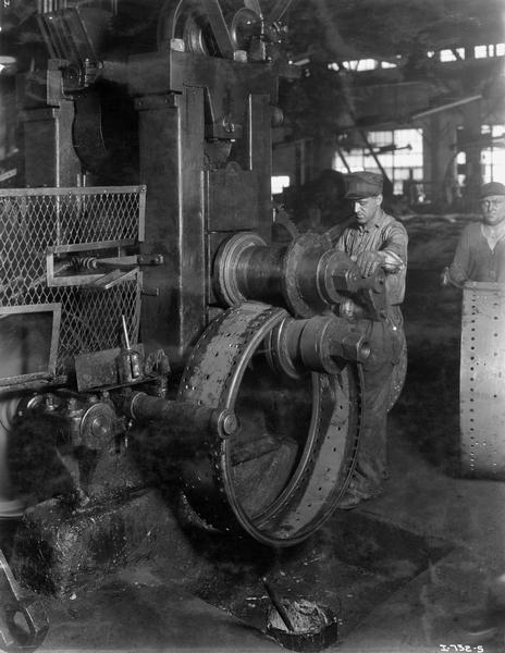 Factory worker uses a roller to shape a tractor wheel at International Harvester's Tractor Works.