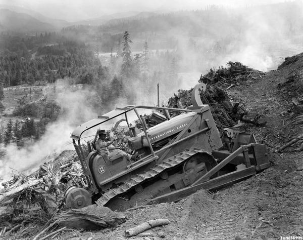 Construction worker clears trees along a hillside with an International diesel TD-24 TracTracTor (crawler tractor).