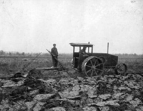 Right side view of men plowing a field with a Mogul 12-25 tractor and a breaking plow.