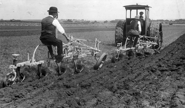 Three well-dressed men are pulling two British made R.Y.L.T. four furrow tractor plows with a Mogul 12-25 tractor. The plows were made by Ransomes, Sims and Jefferies of Ipswich, England. The men are plowing a field in Chelton, Berkshire, England.