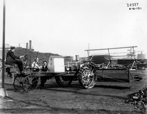 Men maneuver an experimental lightweight tractor designed by John F. Steward through the yard of one of International Harvester's factories - most likely McCormick Works.