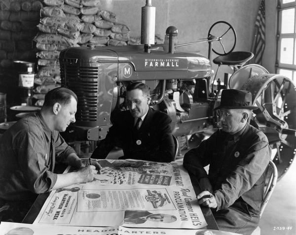 International Harvester dealer Charles Landaal signs a pledge to help collect scrap as part of Governor Julius P. Heil's "MacArthur Week" scrap drive. Milwaukee "blocksman" Dale Thomas (center) and "implement man" Alfred Galler (right) look on. A Farmall M tractor on steel wheels is in the background.