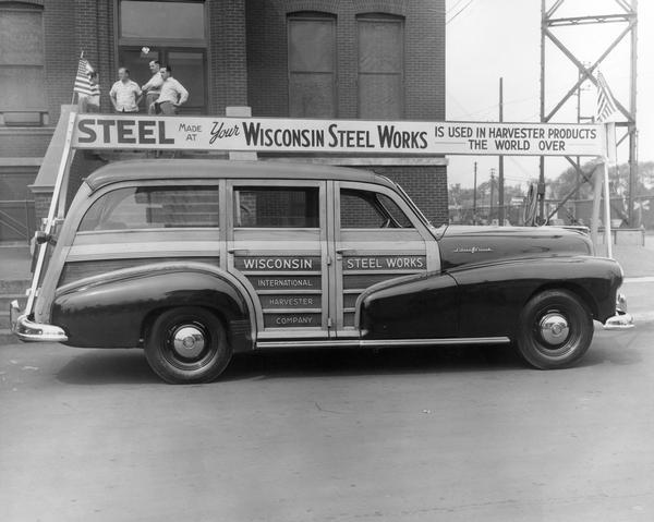 Pontiac Silver Streak station wagon decorated with a Wisconsin Steel Works banner parked along a curb before Chicago's East Side Centennial Parade.