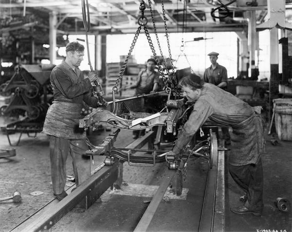 Factory workers attaching a front axle to a truck frame on an assembly line at International Harvester's Fort Wayne Works.