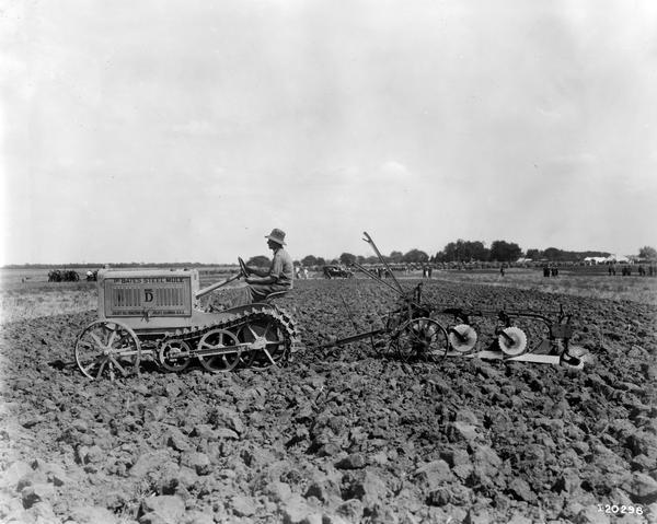 Man pulling a tractor plow with a Bates Steel Mule Model D tractor at what appears to be an agricultural exhibition or fair. The Bates Steel Mule was manufactured by the Joliet Oil Tractor Company of Joliet, Illinois.