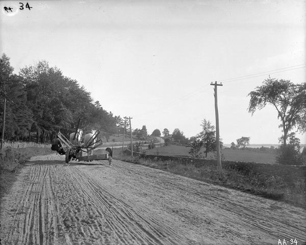 Farmer pulling a McCormick Daisy reaper with two horses down a dirt country road.