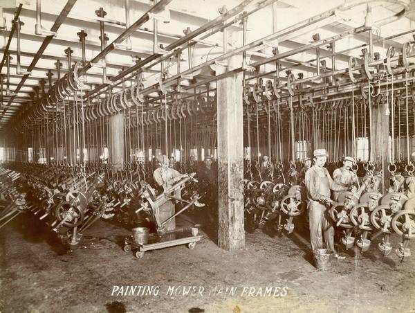 Workers hand painting hundreds of McCormick mower main frames hanging in the McCormick Reaper Works. The factory was owned by the McCormick Harvesting Machine company before 1902. In 1902 it became the McCormick Works of the International Harvester Company. The factory was located at Blue Island and Western Avenues in the Chicago subdivision called "Canalport." It was closed in 1961.