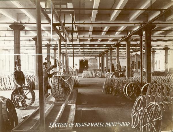 Workers handling mower wheels during painting process in the mower wheel paint shop at the McCormick Reaper Works. The factory was owned by the McCormick Harvesting Machine company before 1902. In 1902 it became the McCormick Works of the International Harvester Company. The factory was located at Blue Island and Western Avenues in the Chicago subdivision called "Canalport." It was closed in 1961.