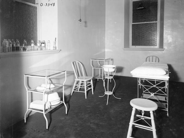 Hospital room at International Harvester's Osborne Works. The room is equipped with an examination table, portable wash basin, wooden chairs, and jars of medical supplies. The factory was owned by the D.M. Osborne Company until 1903, when it was purchased by International Harvester. The factory was later known within the company as the "Auburn Works." It was located at 5 Pulaski Street.