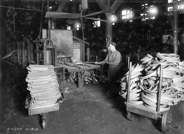 Factory worker removing a harrow spring tooth from a heat treating furnace at International Harvester's Osborne Works. The factory was owned by the D.M. Osborne Company until 1903, when it was purchased by International Harvester. The factory was later known within the company as the "Auburn Works." It was located at 5 Pulaski Street.