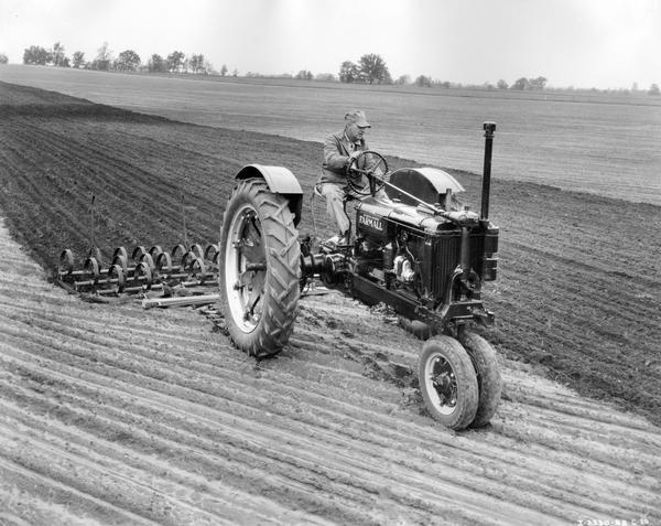 Farmer Charles Hibbard is using his Farmall 14 tractor with attached fourteen section spring harrow to plow a field on his 400-acre farm.