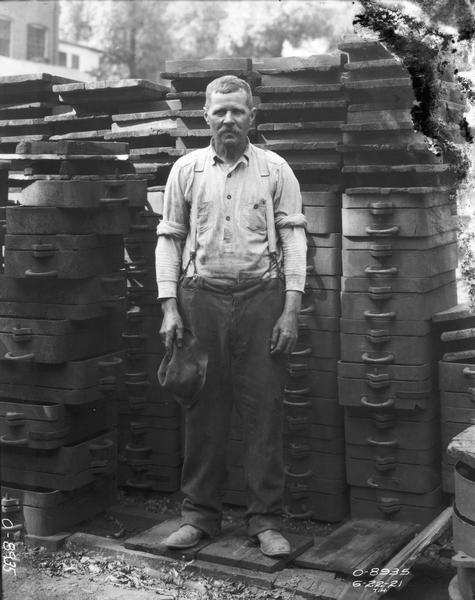 Portrait of an International Harvester employee standing with stacks of part casting molds. The worker may have been employed at the company's Osborne Works.