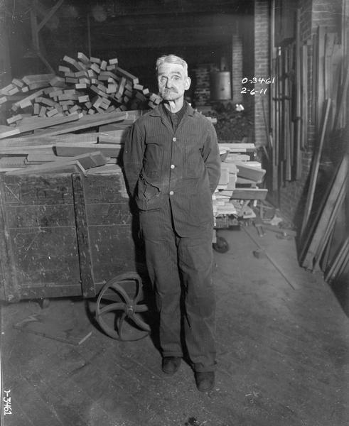 Older worker standing in front of carts loaded with wood in an International Harvester factory (most likely Osborne Works).