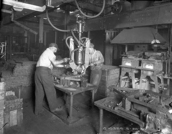 Two International Harvester factory workers using a large pneumatic vise to form frame components. The scene may be at the company's Auburn (formerly Osborne) Works in New York.